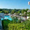 Una piscina con ombrelloni, palme e arbusti in fiore, vista su colline lussureggianti.