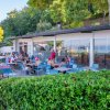 Un gruppo di persone sedute all'aperto in un caffè circondato da alberi e siepi.