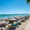 Spiaggia con ombrelloni e lettini lungo la costa, mare azzurro sullo sfondo.