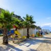 Spiaggia con palme, area giochi per bambini e file di ombrelloni.
