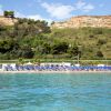 Spiaggia gremita di ombrelloni blu, vicino a una collina verde con alberi.