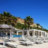 Spiaggia con ombrelloni e lettini sotto un cielo blu, fiancheggiata da palme e una struttura bianca.