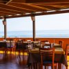 Ristorante con tavoli e sedie in legno, vista mare attraverso un'ampia apertura.
