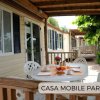 Casa mobile beige con veranda in legno, tavolo apparecchiato per colazione, vista verde.
