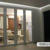 Porta a vetri che dà su un soggiorno con cucina, tavolo e sedie bianche.