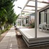 Area con bungalow moderni, terrazze in legno e giardino con alberi e fiori lungo un sentiero.