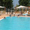 Piscina all'aperto con persone che nuotano, circondata da lettini e ombrelloni.