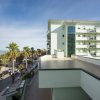Edificio moderno vicino al mare, circondato da palme sotto un cielo sereno.
