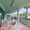 Due persone siedono su un ampio balcone con tavolo e sedie rosa, circondato da palme.
