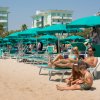 Famiglia su lettini sotto ombrelloni verdi su una spiaggia affollata.