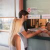 Due persone ricevono un piatto da una finestra in un'area ristoro.