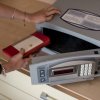 Una persona ripone un portafoglio rosso e bianco in una cassaforte elettronica aperta.