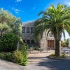 Edificio in pietra con tavolini all'aperto, circondato da palme e vegetazione.