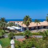 Un complesso turistico con palme, edifici bianchi e uno scorcio di mare blu in lontananza.