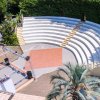 Anfiteatro all'aperto con gradinate semicircolari, circondato da vegetazione.