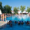 Piscina all'aperto con persone in fila, alcune in acqua, giornata di sole.