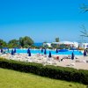 Piscina con lettini e ombrelloni blu, mare sullo sfondo.