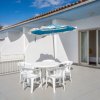Una terrazza con tavolo e sedie bianche sotto un ombrellone blu e bianco.