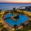 Vista dall'alto di un resort al tramonto, con una grande piscina centrale e giardino.