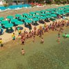 Spiaggia affollata con ombrelloni verdi.