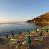 Un tramonto illumina una spiaggia sabbiosa con file di ombrelloni verdi chiusi e sdraio.
