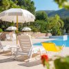 Lettini e ombrelloni bianchi accanto a una piscina azzurra, con vegetazione intorno.