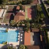 Vista aerea di un resort con piscine, campi da tennis e palme.