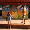 Bambino e adulto su un palco con sfondo colorato, intenti a lanciare oggetti verso un bersaglio.
