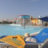 Lettino con asciugamano e cappello vicino a una piscina con fontana, sotto un cielo limpido.