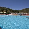 Piscina all'aperto con bagnanti e sedie a sdraio, circondata da colline.