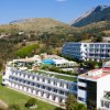 Grande hotel con terrazze, piscina e vista su montagne e colline verdi.