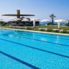 Una piscina con ombrelloni bianchi, prato verde e vista mare sullo sfondo.