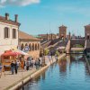 Canale con passerella, ponti in pietra e stand con persone nella città di Comacchio.