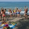 Gruppo di persone in costume da bagno fa stretching su una spiaggia.