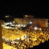 Vista notturna di una fortezza circondata da una folla e tendoni bianchi illuminati.