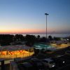Vista serale su un patio con tavolini e vista mare, auto parcheggiate e cielo al tramonto.