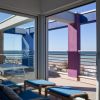 Terrazza vista mare con poltrone blu, tavolini e struttura con elementi colorati.