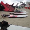 Tavole da surf e vele colorate disposte sulla sabbia di una spiaggia.