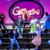 Gruppo di persone in abiti anni '50 che ballano su un palco con l'insegna 