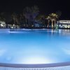 Piscina illuminata di sera con palme intorno e cascata d'acqua.