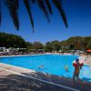 Bambini giocano in piscina con ombrelloni colorati intorno.
