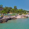 Vista aerea di una spiaggia rocciosa e lettini sotto ombrelloni verdi.