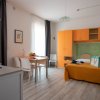 Un monolocale con angolo cottura, letto matrimoniale arancione, tavolo da pranzo e armadi arancioni.