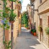 Stradina di un borgo con case in pietra e fiori appesi.