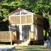 Casa di legno su due livelli con veranda, circondata da alberi.