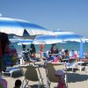 Ombrelloni blu su una spiaggia affollata con persone che prendono il sole.
