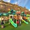 Un parco giochi con scivoli verdi sotto una collina erbosa.