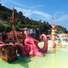 Piscina con struttura a forma di polpo gigante rosa vicino a un faro e ombrelloni arancioni.