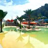 Piscina con scivoli bianchi, ombrelloni arancioni e palme.