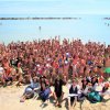 Un gruppo di persone in spiaggia esulta insieme davanti al mare.